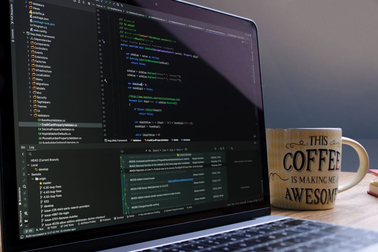 Home Close-up of laptop with coding software and a motivational coffee mug on a desk.