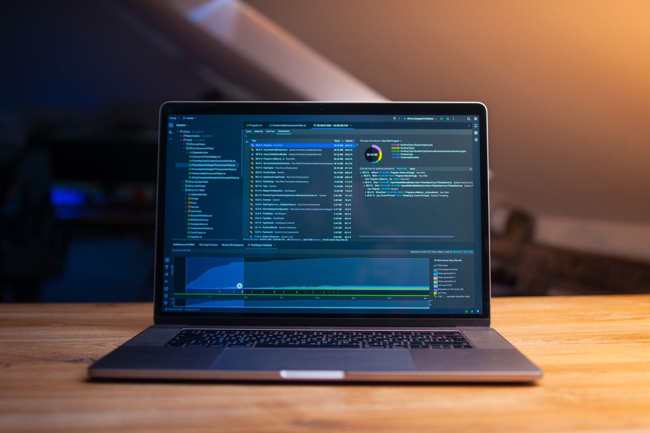 Home A laptop displaying code on a wooden desk, in a dimly lit workspace.