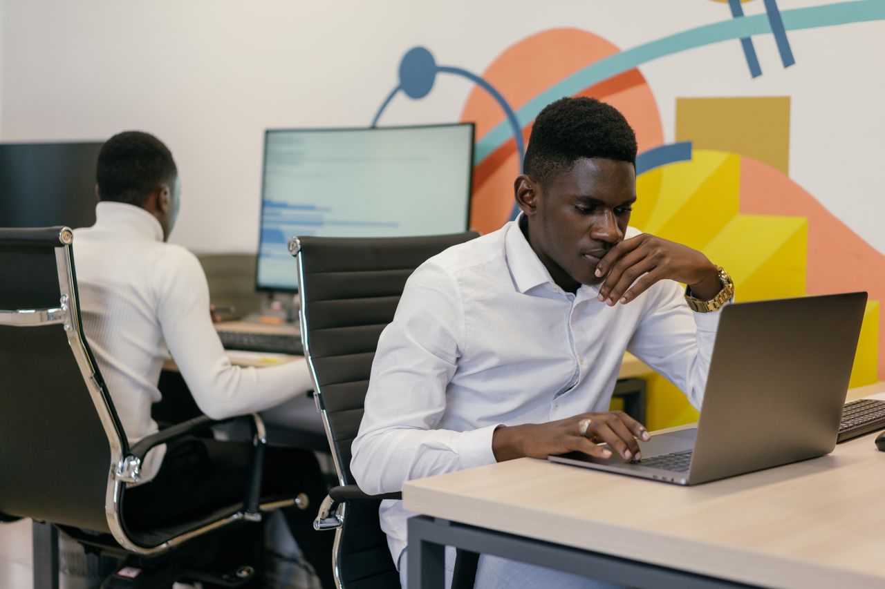 services-02 Two African American men working intently at desks in a vibrant modern office setting.